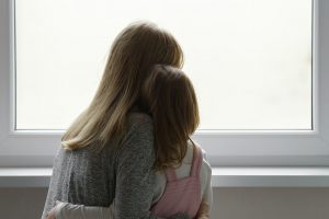 Mother and daughter embrace in front of window