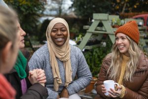 Three young women sit outside with hot drinks