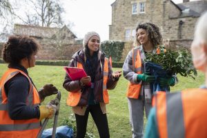 Medium shot of women working together on a community garden outreach project to help improve their local environment. They are wearing hi-vis jackets as they stand together holding pliers, discussing their plan of action in the North East of England.