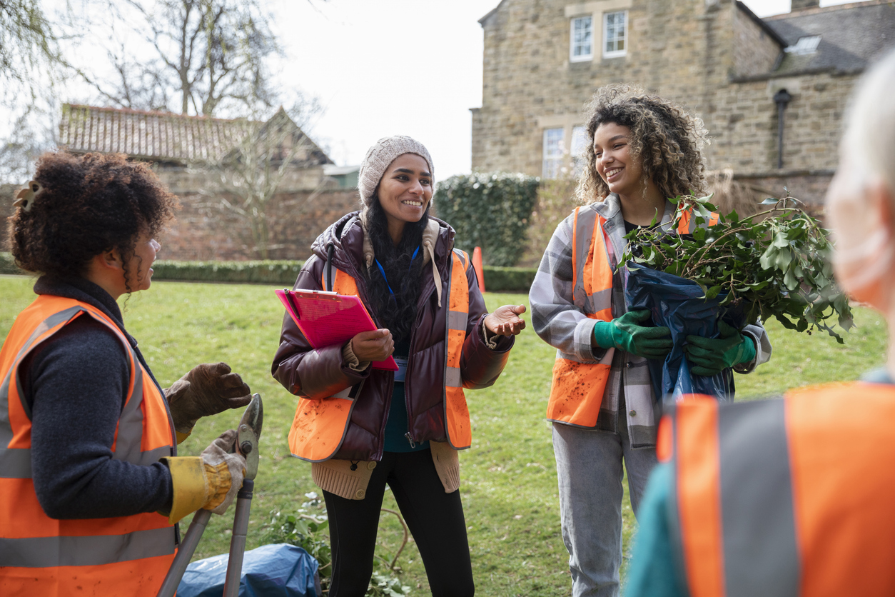 Medium shot of women working together on a community garden outreach project to help improve their local environment. They are wearing hi-vis jackets as they stand together holding pliers, discussing their plan of action in the North East of England.