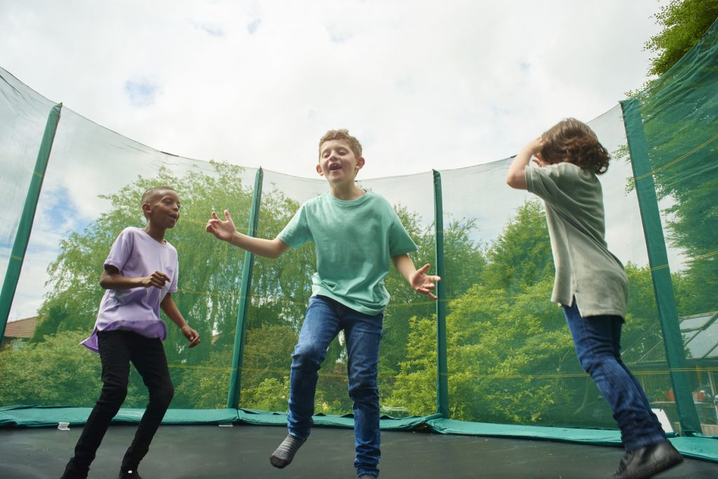 Three children playing on a trampoline in the garden