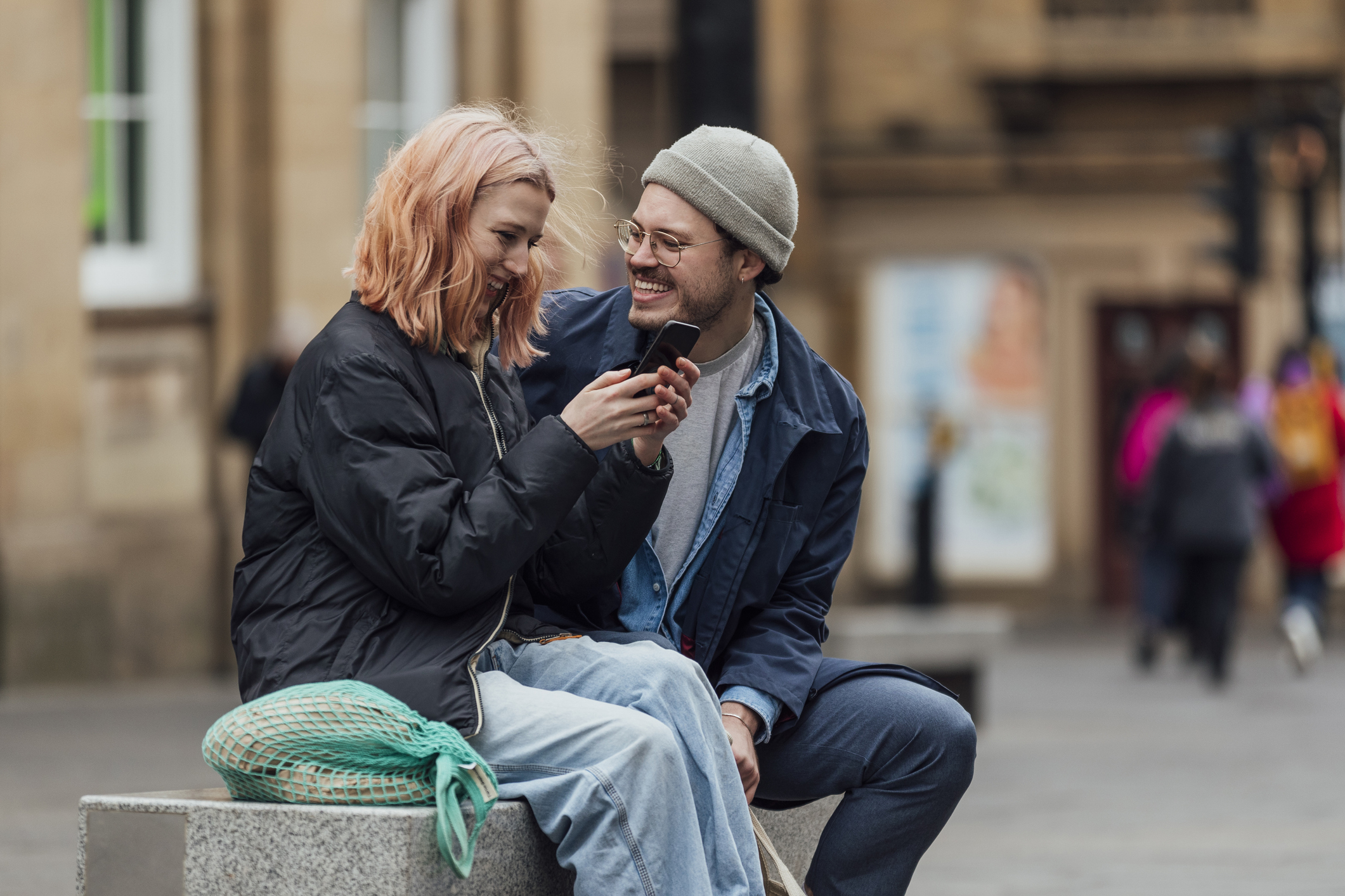 Couple laughing while she looks at her phone in the street