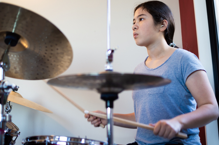 Teenage girl in blue tshirt playing drums